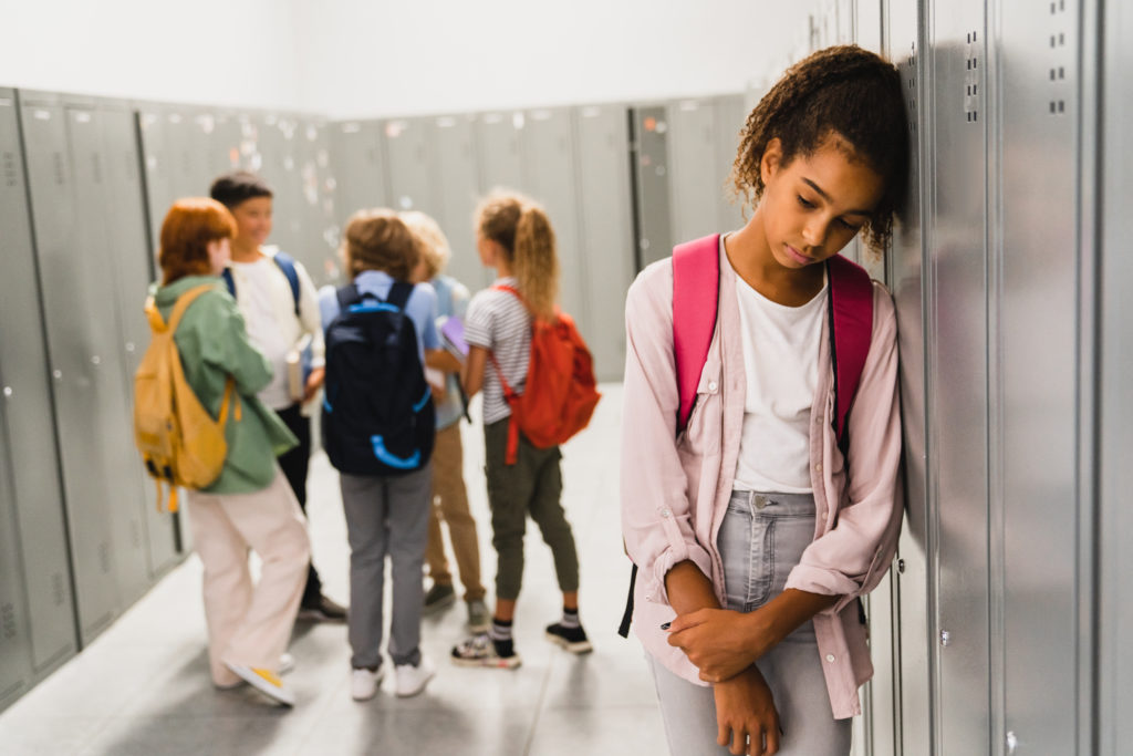 Lonely sad schoolgirl crying while all her classmates ignoring her. Social exclusion problem.
